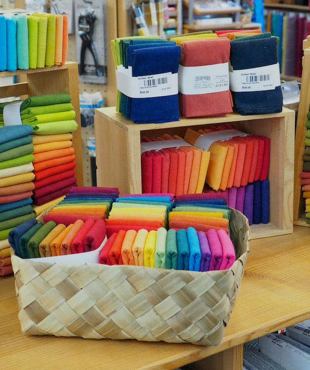 Cherrywood Fabric fat quarter and half-yard bundles displayed on a counter in baskets and boxes